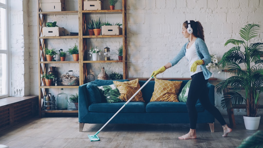 services-02 Cheerful young woman is dancing with mop during routine clean-up in nice loft style apartment, she is listening to music with wireless headphones and singing enjoying her occupation.